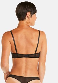 Soutien-gorge en dentelle noire avec bretelles réglables, fermeture à crochets et œillets, et un dos transparent, mettant en avant une texture délicate et une simplicité élégante.
