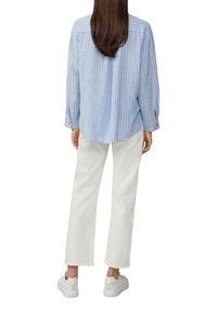 Blauw-wit gestreepte blouse met lange mouwen, met knoopmanchetten, gecombineerd met witte cropped pantalon en witte sneakers. Achteraanzicht.