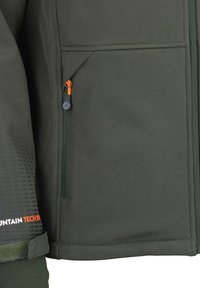 Dunkelgrüne Softshell-Jacke mit einer Reißverschlusstasche und einem orangefarbenen Ziehband, strukturiertem Muster auf der unteren linken Seite und verstärkten Nähten.