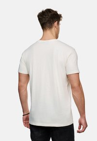 Helles beige T-Shirt mit kurzen Ärmeln, weiche Textur, Rundhalsausschnitt, glatter Stoff. Getragen mit dunklen Jeans, die von hinten eine entspannte Passform zeigen.