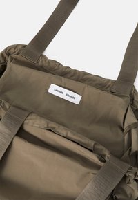 Oliven grønn stoffveske med teksturert overflate, polstret design og to solide stropper. Har en merkelapp sydd inni med merkenavn.
