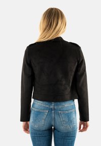 Chaqueta corta de ante sintético negro con mangas largas y hombreras, combinada con jeans de mezclilla ajustados azules que tienen bolsillos traseros.