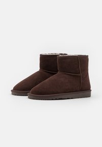 Brown suede ankle boots with a soft interior lining, rounded toe, and a flat rubber sole, featuring stitched detailing and minimalistic design.