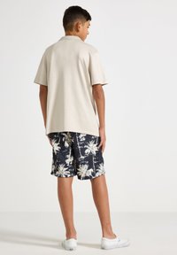 Beige kortärmad pikétröja i kombination med svarta shorts med vita palmträdsmönster. Vita sneakers fulländar outfiten.