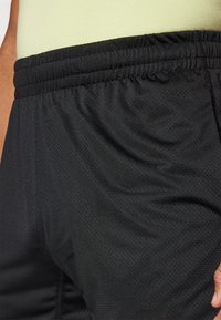 Calções atléticos pretos feitos de um tecido leve e texturizado, com uma cintura elástica. Inclui costuras visíveis e um design de corte descontraído.