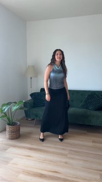 Fustă maxi neagră asortată cu un top fără mâneci de culoare gri-albastră. Decorul include o canapea verde, o plantă de apartament și un podea din lemn.
