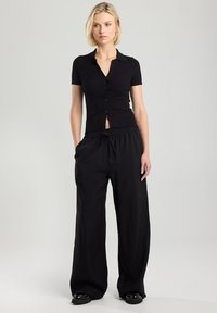 Black ribbed knit short-sleeve shirt with a button front and slight opening. Relaxed black wide-leg trousers with an elastic waistband.