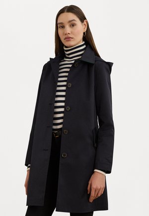 Cappotto blu scuro con colletto, chiusura a bottoni e tasche laterali. Presenta un'accents verde sul colletto e un tessuto liscio e strutturato.