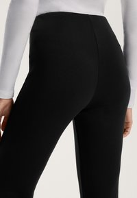 Leggings noirs en tissu extensible, avec une taille haute et une texture lisse. Le design comprend une silhouette ajustée qui épouse le corps.