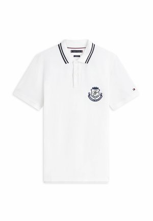Polo bianca a maniche corte con doppie strisce nere sul colletto, due bottoni bianchi, stemma Tommy Hilfiger blu navy sul petto e piccolo logo sulla manica.