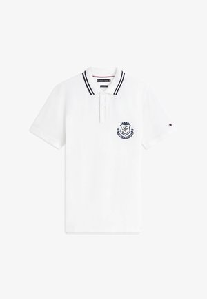 Polo bianca a maniche corte con doppie strisce nere sul colletto, due bottoni bianchi, stemma Tommy Hilfiger blu navy sul petto e piccolo logo sulla manica.