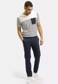 T-shirt z krótkim rękawem w paski z granatową kieszenią; zestawiony z granatowymi spodniami i białymi trampkami. Materiał bawełniany, luźny krój, nowoczesny design.