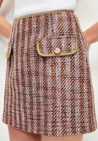 Tweed mini skirt featuring a brown, pink, and white pattern, with green trim and two front pockets adorned with gold-tone buttons.