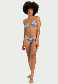 Τρίγωνο μπικίνι με μπλε και πράσινο σχέδιο υφάσματος; λεπτές τιράντες; αντίστοιχα χαμηλοκάβαλα σλιπ; λεία υφή; λεπτομέρειες διακριτού φυλετικού σχεδίου.