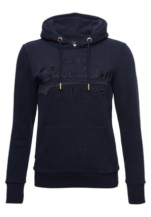 Granatowa bluza z kapturem z przednią kieszenią, ściągaczami ze sznurkiem zakończonym metalowymi końcówkami oraz haftowanym napisem "Real SuperDry" z japońskimi znakami na piersi.