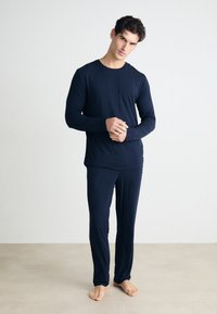 Tengerészkék, hosszú ujjú felső kerek nyakkivágással és hozzáillő nadrág, mindkettő puha, sima anyagból készült, slim fit fazonban és minimális dizájnnal.