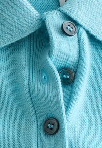 Gros plan d'une chemise tricotée bleu clair montrant trois boutons foncés et un col en tissu texturé.