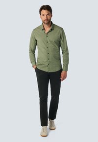 Grünes karierter Hemd, Slim Fit, langärmlig; kombiniert mit dunklen Hosen und hellen Sneakers. Verfügt über schwarze Knöpfe und eine glatte Textur.