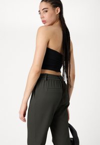 Haut noir sans bretelles avec texture froncée, associé à un pantalon côtelé vert foncé doté d'une taille élastique et d'une poche latérale.