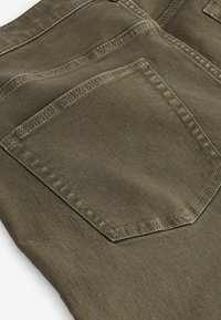 Gros plan sur un tissu vert olive avec un détail de poche arrière à double surpiqûre sur un pantalon décontracté ou un jean.