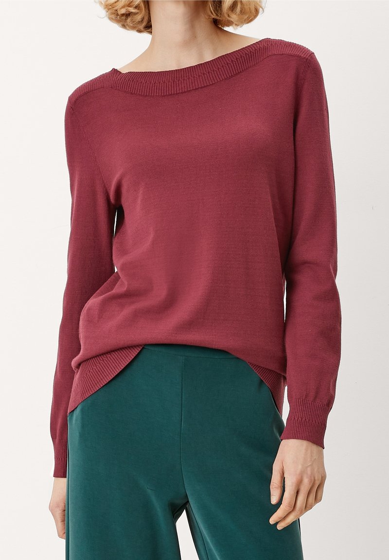 Pull en maille bordeaux avec un large col bateau et un ourlet à côtes, associé à un pantalon vert foncé, offrant une coupe décontractée et des manches longues.