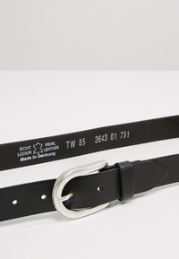 Schwarzer Ledergürtel mit einer silbernen Metallschnalle. Auf der Innenseite sind Maße und Text angebracht, die das Material und die Herkunft angeben.
