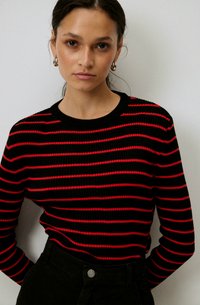 Svart och röd randig stickad tröja med rund halsringning, ribbad textur och figursydd design, i kombination med högmidjade svarta byxor.