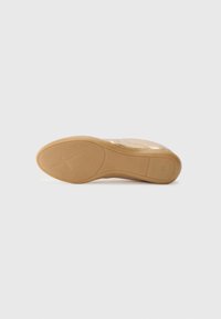 Light golden shoe with a textured surface and a flexible, tan rubber sole featuring a cross pattern and subtle branding on the bottom.