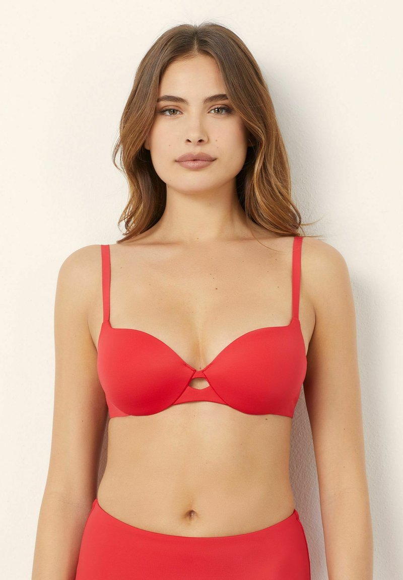 Seno rosso push-up con coppe lisce, spalline sottili e regolabili, e un piccolo dettaglio a taglio al centro. Tessuto morbido e elastico.