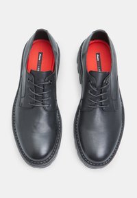 Une paire de chaussures en cuir noir à lacets avec des semelles épaisses et des semelles intérieures rouges étiquetées "Bata Red Lab" sur un fond blanc.