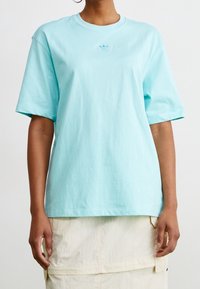 Ljusblå t-shirt i bomull med kort ärm, avslappnad passform och liten broderad logotyp på bröstet. Slät textur.