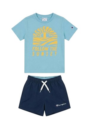 Camicia azzurro chiaro a maniche corte con grafica di sole giallo e testo "Follow the Sunset", abbinata a pantaloncini blu navy con coulisse bianca.