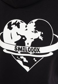 Haut à capuche noir avec un graphique blanc représentant un globe en forme de cœur, avec le texte "SMILODOX" en dessous, mettant en avant des continents et un design orbital.