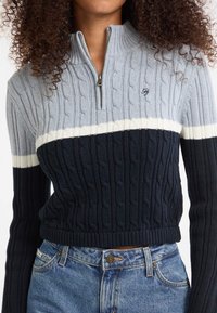Maglione a maglia con zip a un quarto, caratterizzato da una combinazione di strisce grigio chiaro, crema e blu scuro. Polsini e orlo a coste, motivo testurizzato su tutta la superficie.
