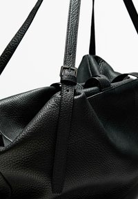 Black leather bag with a textured finish, featuring adjustable straps and a structured design. Notable buckles and stitching details.