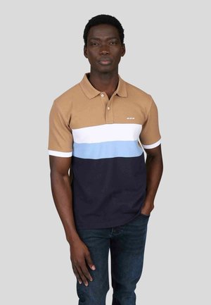 Polo à manches courtes dans des tons beige, blanc, bleu clair et rayures bleu marine. Présente un col et un patte de boutonnage à trois boutons. Porté avec un jean foncé.