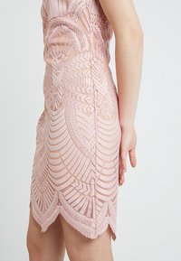 Robe en dentelle rose présentant des motifs de feuilles en relief complexes, une silhouette ajustée et un ourlet festonné. Texture lisse avec des éléments transparents.