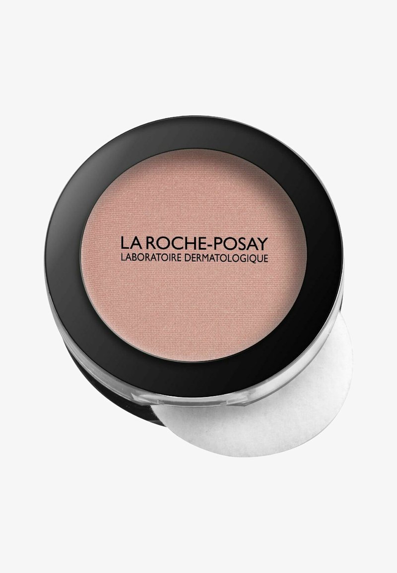 Kompakter Puder in einem runden schwarzen Gehäuse mit weißen und klaren Akzenten; enthält weichen rosa Puder mit glatter Textur und Logo.