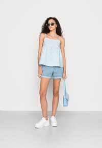 Top sem mangas de cor azul clara com um padrão texturizado, combinado com calções de ganga, ténis de plataforma brancos e uma mala azul clara.