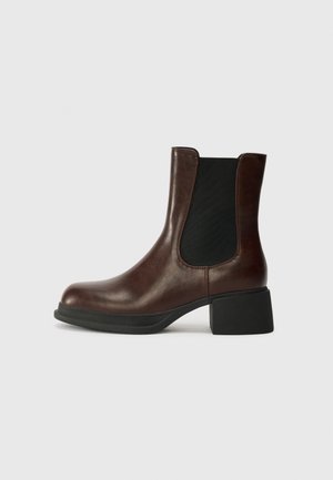 Bottine en cuir marron avec un bout arrondi, un panneau latéral élastique et un talon épais noir. Texture lisse avec un design minimaliste.