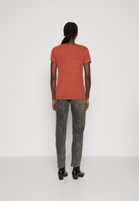 Tričko s krátkým rukávem v barvě rezavé, uvolněný střih, spárováno se šedými slim-fit kalhotami a černými kotníkovými botami na podpatku. Jednoduchá, texturovaná látka.
