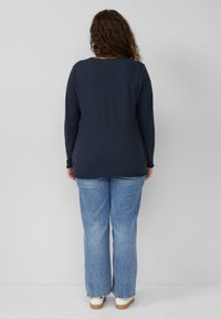Marineblaues Langarmoberteil mit rundem Ausschnitt und lockerer Passform, kombiniert mit hellblauen Schlagjeans und weißen Sneakers. Weiche Stoffstruktur.