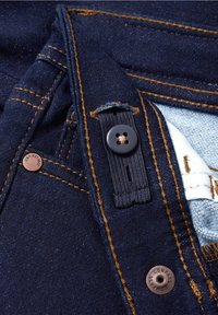 Jean en denim bleu foncé avec rivets en cuivre visibles et coutures orange, mettant l'accent sur le bouton, la boutonnière et les détails du tissu intérieur.