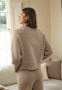Beige gebreide trui met een verkorte zoom, geribbelde manchetten en een licht oversized pasvorm, gedragen met bijpassende onderstukken in een zachte stof.