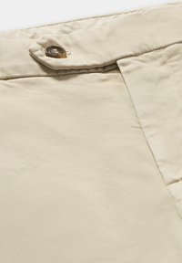 Béžové bavlněné kalhoty s knoflíkovým zapínáním, hladkou texturou a čistým designem, se zaměřením na pas a detail látky.