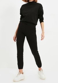 Zwarte sweatshirt en jogger outfit gemaakt van zachte stof, met een elastische tailleband en boorden, gecombineerd met witte sneakers.