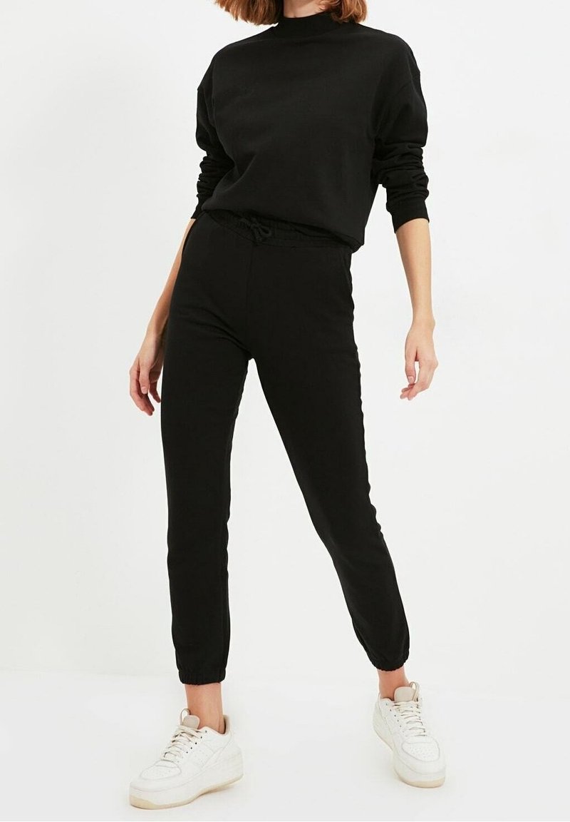 Zwarte sweatshirt en jogger outfit gemaakt van zachte stof, met een elastische tailleband en boorden, gecombineerd met witte sneakers.