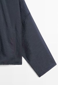 Lång ärm på mörkblå lätt jacka som visar textur och söm detaljer på tyget mot vit bakgrund.