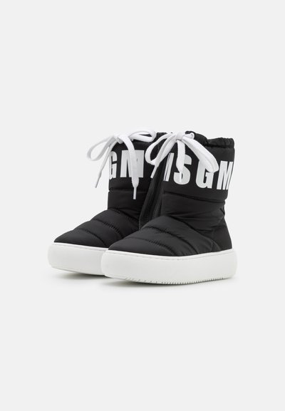 Botas de tornozelo acolchoadas pretas com sola de borracha branca, atacadores brancos e um logótipo preto e branco proeminente no cano. Detalhes de superfície texturizada.