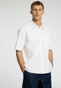 Camicia bianca a maniche corte con taschino, realizzata in tessuto leggero. Presenta un colletto classico e una vestibilità rilassata.